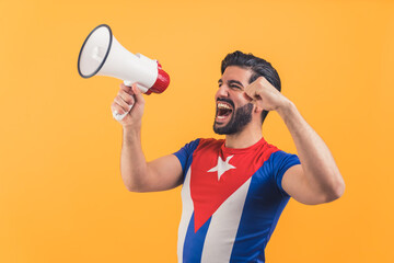 excited Latin man in the T-shirt of Cuban flag celebrating something and holding a megaphone and shouting orange background medium shot studio shot celebration concept. High quality photo