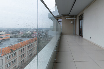 Large spacious balcony in a new house in rainy weather. Interior of a bright empty balcony in the house glass railings.