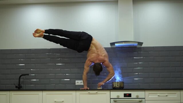 Man keeps balance on one hand and cooks food in the kitchen. Concept of willpower, motivation and passion