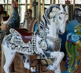 Fototapeta na wymiar Carved white and black spotted horse with saddle and white roses on a carousel ride
