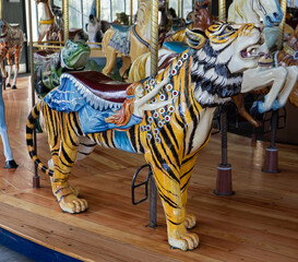 Fototapeta na wymiar Carved carousel figure of a saddled tiger surrounded by other carousel figures. A woman clinging to bejeweled chains is depicted on its side.
