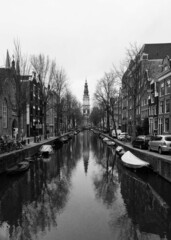 The Zuiderkerk (South Church) in Amsterdam reflected in an Amsterdam canal in black and white. Amsterdam houses line the canal and boats are in the canal. © Tatum