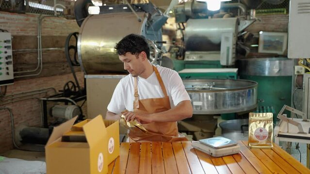 young man who owns a small coffee roaster and a young start-up is packing the finished coffee beans into bags and boxes.
