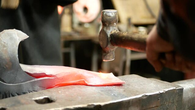Two blacksmiths use hammers to make a decorative pattern on the workpiece