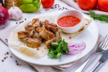 Kebab from lamb ribs with tomato sauce and red onion on white plate