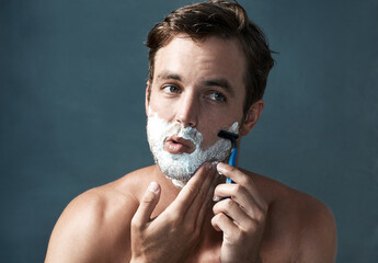 Keeping a clean shave. Cropped shot of a handsome young man shaving against a grey background.