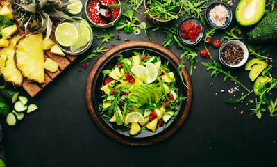 Vegan vegetarian salad with pineapple, arugula, avocado and dried cherry on black plate on dark stone kitchen table, top view. Healthy eating, clean diet food, weight loss concept