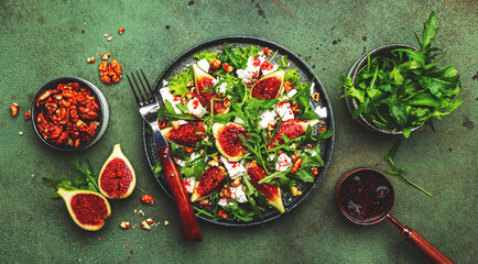 Delicious summer salad with figs, feta cheese, walnuts, arugula and sweet  jam dressing on rusty green table background, top view, negative space