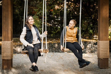 Obraz premium A young man with his lover are sitting on a swing in the forest among the trees.