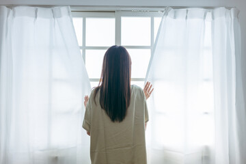 窓を開けるミドル世代の女性（起床）
