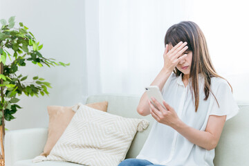 ソファに座るミドル世代の女性（落ち込む）

