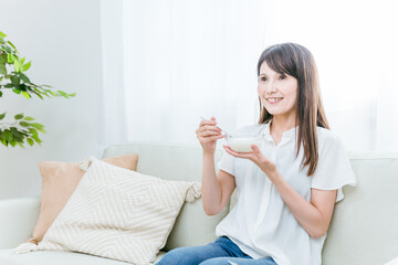 Obraz na płótnie Canvas ソファでヨーグルトを食べる女性（笑顔） 
