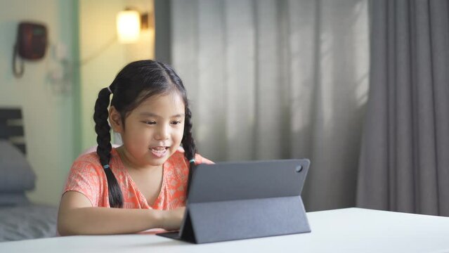 Asian Child Happy Smile Talking Fun To Teacher Via Video Call Learning On Computer Tablet Or Kid Girl Student Enjoy Laughing And Studying Online Class Or Person Learn From Home School In Bedroom