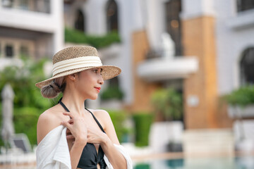 Woman wearing black dress and straw hat relaxing by the pool.