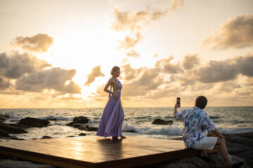 Couple in love man taking photo woman on the beach, enjoy sunset romantic moment.