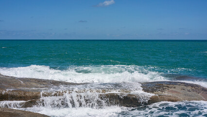 Fototapeta na wymiar Rocky beach with white waves, deep blue ocean views and blue sky.