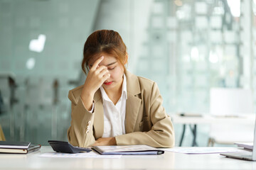 Overworked and stressed young Asian woman sitting at workplace in office.