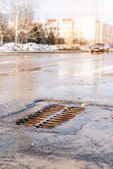 The rusty grate of the storm sewer after the rain. The water drains into the storm drain. Urban landscape in the background