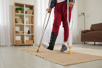 Unrecognizable person with broken foot walking on crutches. Athlete wearing leg brace ankle support adjustable strap fracture fixator trying to walk at home. Cropped low section shot. Injury concept