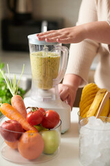 Woman making delicious smoothie for breakfast at kitchen table