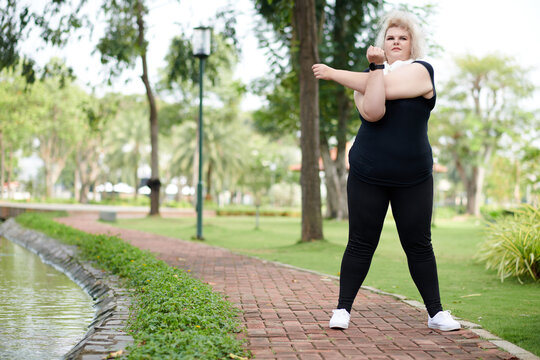 Curvy young woman warming up before morning run in park