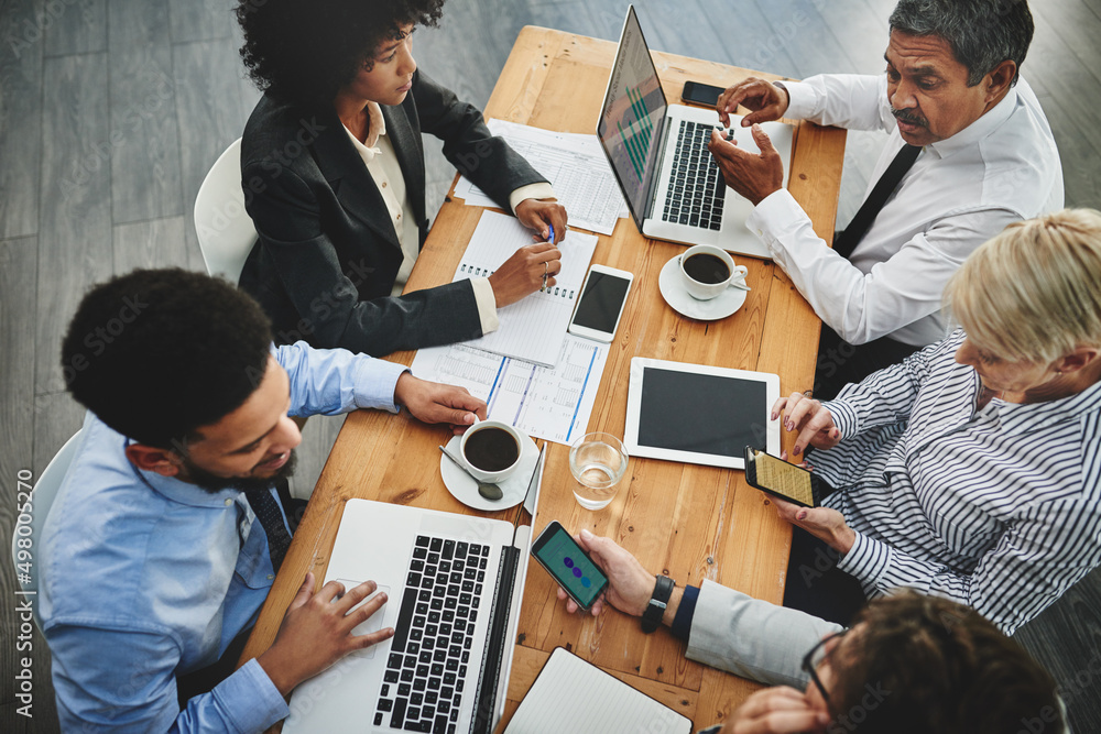 Poster working from their multiple devices. shot of a group of businesspeople having a meeting in an office
