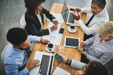 Working from their multiple devices. Shot of a group of businesspeople having a meeting in an...