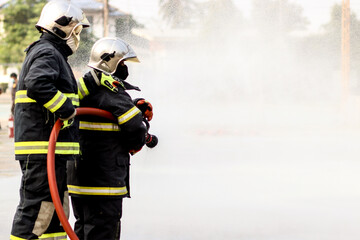 Fototapeta premium Firefighters using Twirl water fog type fire extinguisher to fighting with the fire flame from oil to control fire not to spreading out. Firefighter and industrial safety concept.