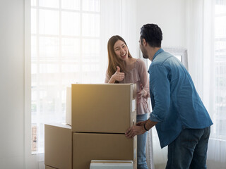 Pretty woman giving thumbs up to man for carrying boxes. Wife showing sign of good job to strong husband for carrying all boxes when moving house.