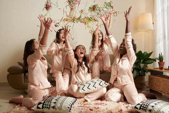 happy excited friends shouting and throwing serpentine ribbons when enjoying pajamas party