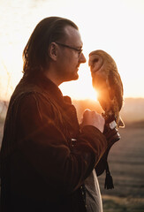 Man and wild bird over sunset sky in field looking on each other Owl symbol of power, wisdom...