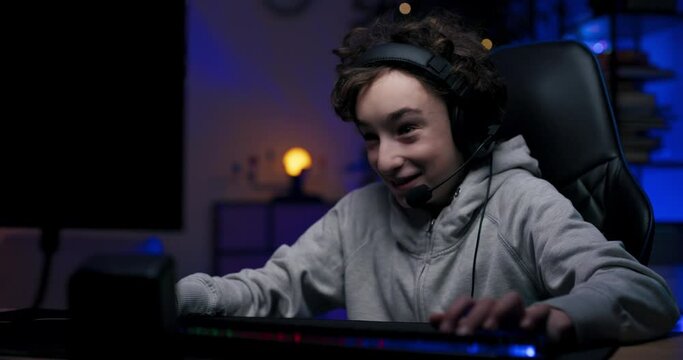 A child addicted to computer games at a young age. College-age boy sits in front of computer at night playing shooters, video game, talking through headset with team members.