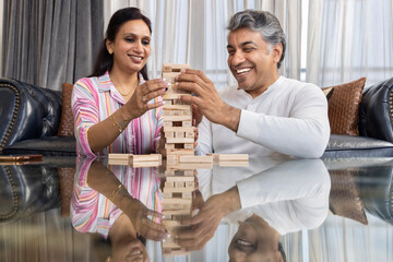 Husband and wife having fun playing wooden blocks stack tower game at home