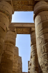 Fototapeta premium Ancient Egyptian hieroglyphs and symbols carved on columns of the complex of Karnak temple. Tall columns against blue sky. Great Hypostyle Hall at Temples of Karnak (ancient Thebes). Luxor, Egypt
