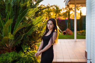 Young beautiful woman in stylish black dress posing outdoor at sunset.
