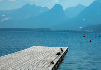 Panoramic view of an austrian lake with wooden pier and mountain range in the background....