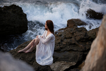 barefoot woman in white dress sits on a cliff nature top view