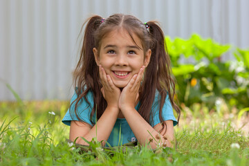 Adorable smiling brunette girl with two tails lies on the green grass, in the summer garden