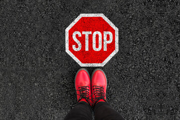 woman legs in boots standing on asphalt road and stop sign