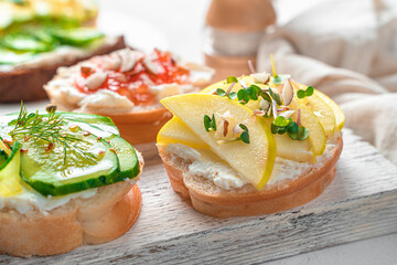 Crostini with ricotta, apple and micro-greenery, feta, cucumber and dill on a light background.