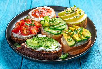 A set of sandwiches with feta, ricotta, vegetables and fruits on a blue background.