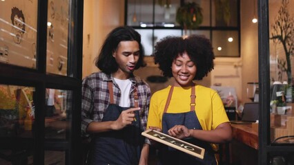Young  couple asian man and african woman manager in restaurant with digital tablet or notebookWoman coffee shop owner with face mask hold open sign .Small business concept.
