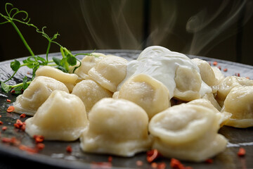 Ukrainian dumplings with sour cream and microgreen, on a black glossy plate, on a dark background
