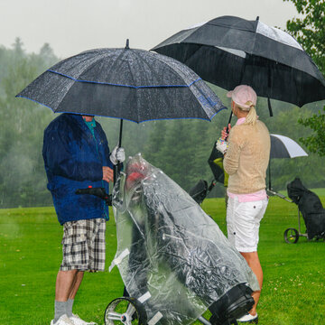 Golfspieler unter schützenden Regenschirmen im Regenschauer
