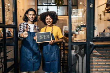 Young  couple asian man and african woman manager in restaurant with digital tablet or notebookWoman coffee shop owner with face mask hold open sign .Small business concept.