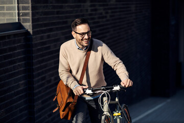 A happy man pushing a bicycle uphill on the street.