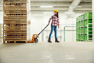 A female factory worker pulling forklift with crates around facility.