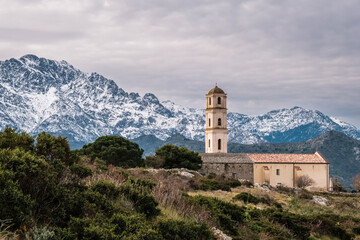 Fototapeta na wymiar Church in the hilltop village of Sant'Antonino in the Balagne region of Corsica with snow capped mountains in the distance