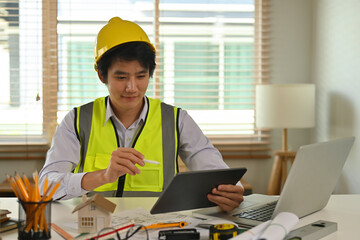 A portrait of a foreman engineer or architecture working on a tablet with tools and machine on the table in the office, for engineering, architect, business, safety and technology concept.