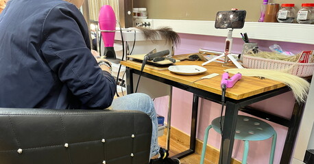 A person sitting in a black leather chair in the hair salon. Process of wig creation. Accessories....
